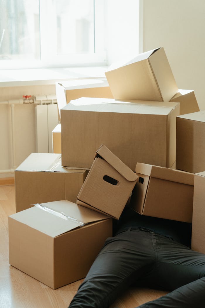 A person buried under a pile of cardboard boxes during a home move, depicting exhaustion.